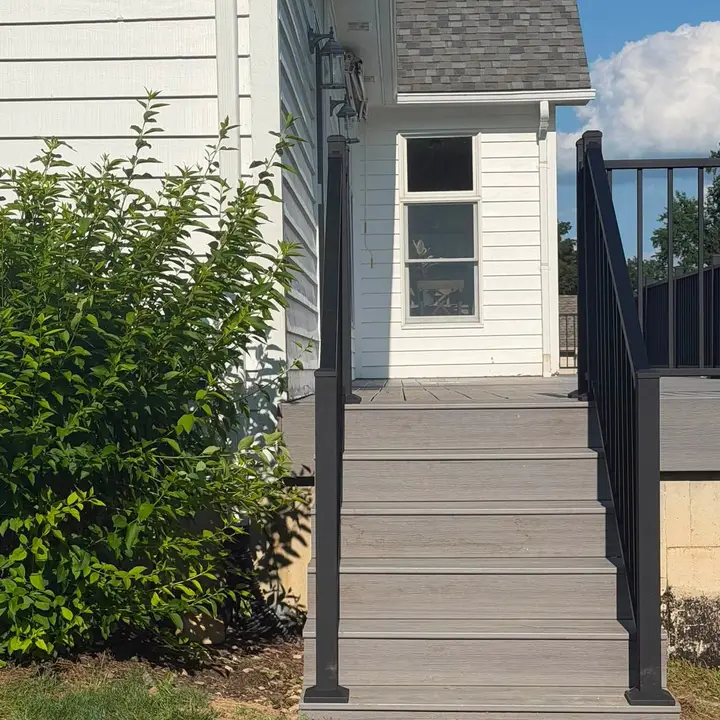 Composite deck steps with a black aluminium handrail, beside a white house.
