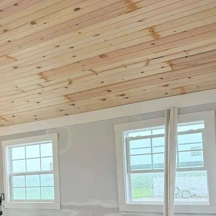 A pine plank ceiling above newly trimmed windows in a room finished to paint stage.